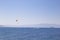 A man flies on a paraglider over the sea, following a boat that
