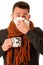 Man with flu and fever wrapped in scarf holding cup of healing t