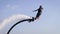 Man is flying on flyboard over sea surface, water flows are lifting him up in summer day, drops are splashing around