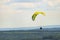 A man flying a green paraglider over a forest on a cloudy day.