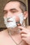 Man with foam on face shaves beard cheek with razor. Close-up portrait, looks in mirror. Male facial care concept at home