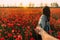 Man follows a woman in poppy meadow at sunset.