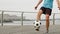 Man footballer is juggling a ball with his feet on waterfront, legs close-up.