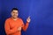 Man forty years old latino with orange sweater points with his hands blue background copy space with happy and natural expression