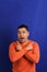 Man forty years old latino with orange sweater points with his hands blue background copy space with happy and natural expression