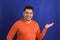 Man forty years old latino with orange sweater points with his hands blue background copy space with happy and natural expression