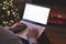 Man freelancer in santa claus hat working on laptop with graphs and charts on screen sitting near christmas tree and fireplace.