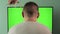 A man in front of a chroma key green screen TV is watching TV. Removing noodles from the ears of viewers. The concept of