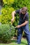 Man gardener in protective clothes with garden shears, scissors or secateurs cutting a boxwood topiary hedge in the garden