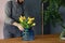 Man with gardening passion putting yellow tulips and blue vase o