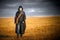 A man in a gas mask walks through a scorched field. He holds a radiometer in his hand