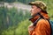 Man geologist with a backpack and a geological hammer in hand against the backdrop of a wooded mountain landscape