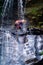 Man gets wet looking down while abseiling down slippery rock face under a cascading waterfall hanging from a rope in wetsuit,