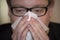 Man with glasses blows his nose with handkerchief