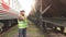 A man in glasses worker checking the train in a helmet and uniform, walking on the railway station talking on the phone