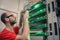 A man with glasses works in the server room. Young engineer switches wires in a rack with telecommunication equipment. The