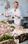 Man in glove behind counter shows fish in his hand