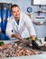 Man in glove behind counter shows fish in his hand