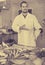 Man in glove behind counter shows fish in his hand