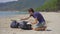 Man in gloves collects plastic trash on a beach. The problem of garbage on the beach sand caused by man-made pollution