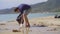 Man in gloves collects plastic trash on a beach. The problem of garbage on the beach sand caused by man-made pollution