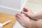 A man with glue glues floor MDF plinth.A man sets up white floor moldings in an apartment.Close view of man installing new skirtin