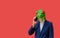 Man with googly-eyed frog mask calling with smart phone on red background