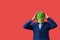 Man with googly-eyed frog mask surprised with his hands on his head on red background