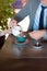 A man in a gray business suit and tie is sitting at the table and pouring tea from the brewer.