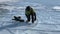 A man in a green jacket, black helmet and red knee pads puts on skates to skate on ice.