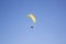 A man on a green orange white paraglider in a gondola against a clean blue sky