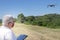 Man with grey hair flying a drone on a field with a tablet and a safety face mask. New normality concept