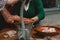 Man grinding meat with an old fashioned grinder on a wooden table with a person on the background