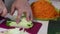 A man grinds a vegetable marrow. Nearby vegetables for cooking squash caviar. Zucchini, carrots, onions and tomatoes on the table