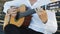 Man guitarist plays guitar outdoors. Musician plays a classical guitar in the park. A man in a white shirt plays a musical