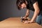 A man hammers nails into a cupboard. The back wall of the cupboard is made of thick cardboard