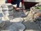 A man hammers paving slabs in a dry sand-cement mix with a rubber mallet. Part of the body of a worker among the piles of tiles