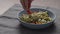 man hand add cherry tomatoes to green fettuccine with pesto in blue bowl