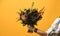Man hand hold modern bridal bouquet with exotic flowers green leafs thistle eryngium on yellow background