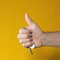 man hand holding house keys on yellow background. makes thumbs up gesture, concept of successful real estate transaction