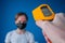 Man hand holding pyrometer, measuring temperature of woman in medical face mask