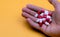Man hand holding red-white capsule pills on yellow background. Prescription drug. Pharmaceutical business. Drug overdose. Health