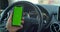 Man hand holding a smartphone with green blank screen in the electric car for direction, massage, location, business