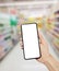 Man hand holding smartphone in Supermarket. Blurred background. Blank white screen for your text.