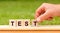 Man hand holding wooden cube block with TEST word on green lawn background. Test, beliefs and agreement concept