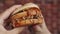 Man hand holds burger with maggots, bites and eats it, closeup. Man holds burger with maggots crawling on it and eats