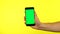 Man hand holds a smartphone with green screen over a yellow background.