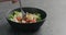 Man hand pick salad with mozzarella, cherry tomatoes and frisee leaves in black bowl on terrazzo surface