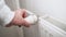 Man hand regulates temperature knob of heating radiator to reduce heating costs.