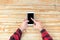 Man hand touch on a screen of mobile phone on a wooden table.